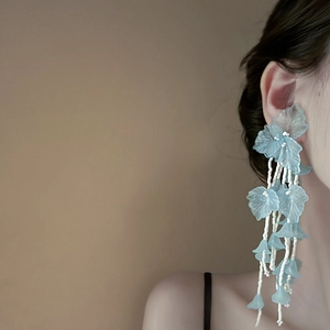 Orecchini a nappa con petali blu e perline bianche su modella, elegante stile foresta