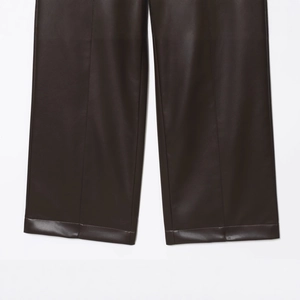 Dettaglio dei pantaloni dritti in ecopelle marrone scuro con cuciture rifinite a mano