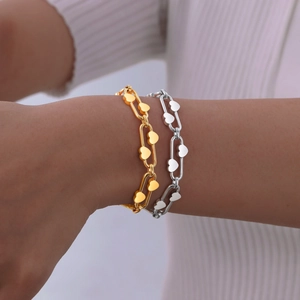 Close-up of gold and silver heart-shaped paperclip chain bracelets on a wrist