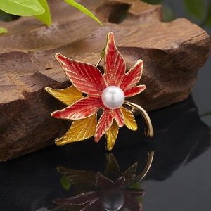 Macro view of a gold-plated maple leaf brooch with red-yellow enamel and a central pearl
