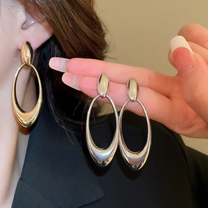 Close-up of model wearing large oval hollow drop earrings with mirror polished finish