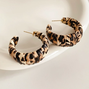 Detailed close-up of C-shaped leopard print earrings with woven texture on a white tray