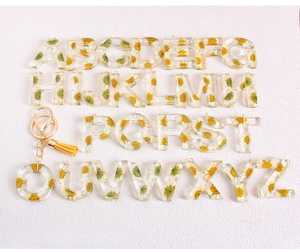 Macro detail of resin letter O keychain with white dried daisy flower and yellow tassel