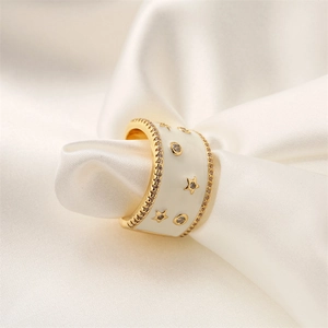 Dettaglio macro di un anello largo dorato con smalto bianco e zirconi a stella