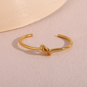 Macro detail of gold-plated knot bracelet with polished mirror finish on pink surface