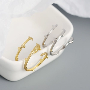 Macro detail of gold and silver S925 rings with natural branch textures on a ceramic dish