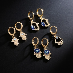 Golden Hamsa Hand earrings with blue evil eye and zircon crystals set on dark background