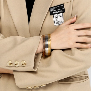 Wrist detail of layered gold, silver and rose gold bangles worn with a beige suit
