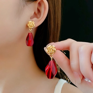 Detail of gold rose stud earrings with red faceted water drop glass pendants on model