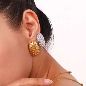 Close-up of gold and silver textured oval stud earrings worn by a model