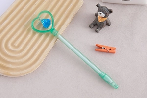 Detail of green heart magic wand pen featuring a blue diamond pendant on textured surface