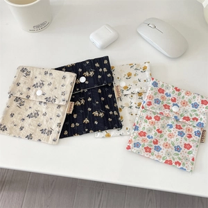 Detailed view of floral sanitary pouch set with snap buttons and woven label on a desk