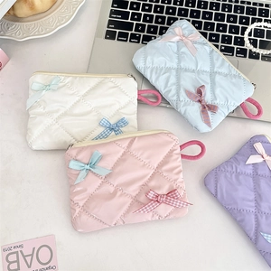 Flat lay of quilted pearlescent cosmetic bags in four pastel colors with bow details