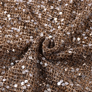 Macro view of silver sequins on brown mesh fabric with shimmering light reflections