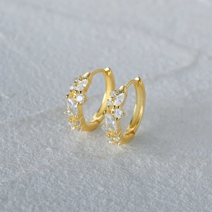 Macro shot of gold hoop earrings with clustered marquise zirconia on stone background