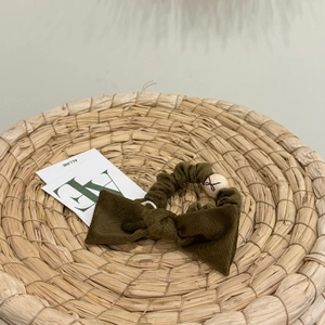 Olive green fabric scrunchie with bow detail and wood bead on a woven mat base