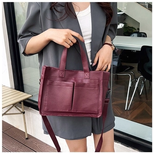 Detail of burgundy PU leather tote bag with front pockets on a casual model outfit