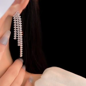 Close-up of sparkling silver tassel earrings with rows of diamonds on a model