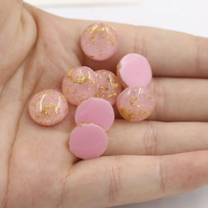 Close-up of pink oval synthetic opal resin cabochons with gold foil flakes on a palm