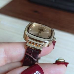 Close-up of a women's square gold watch with brown leather strap and crystal accents
