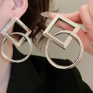 Close-up of geometric silver metal earrings with square and circular interlocking design