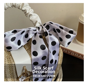 Close-up of straw apple bag featuring silk scarf detail and gold floral pendant