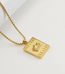 Détail d'un pendentif doré rectangulaire avec relief couronne et motifs lune et étoile