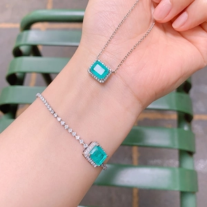 Macro shot of silver jewelry set with emerald-cut green gemstones and diamond halos
