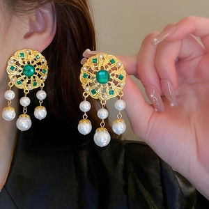 Detailed view of vintage gold earrings with green gemstones and elegant pearl drops