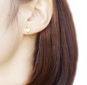 Close-up of a minimalist gold heart stud earring worn on a model's ear with a polished finish