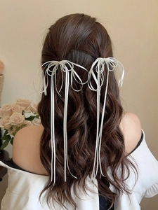 Elegant white ribbon bow hair clip with pearl beads and long tassels on wavy brown hair