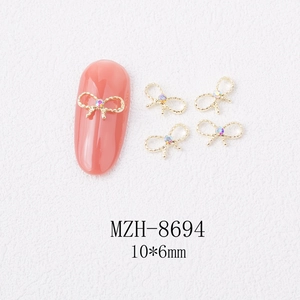 Macro detail of 10x6mm golden bow nail charms with iridescent gems for nail art decor