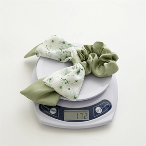 Detail view of a floral green bow hair tie weighing 17.2g on a white digital scale