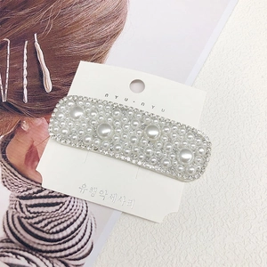 Detail of a rectangular hair clip featuring inlaid pearls and small crystals on a card