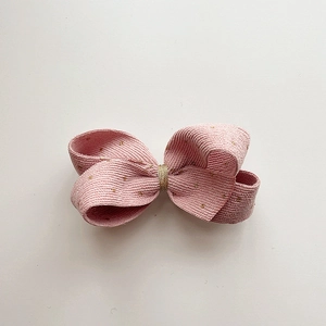 Detailed view of pink corduroy bow hair clip with gold polka dots and woven texture