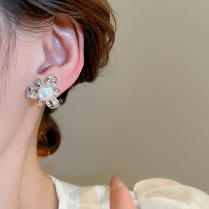 Detailed view of silver bow pearl stud earring with sparkling zircon on model's ear