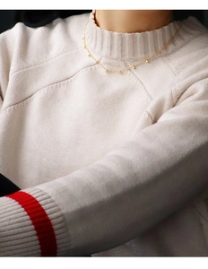 Detail of a minimalist gold-plated necklace with zircon beads worn on a beige knit sweater