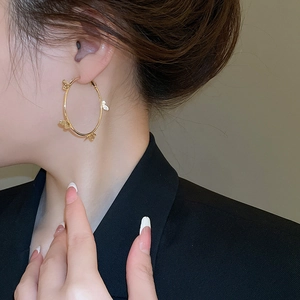 Close-up of elegant gold hoop earrings with butterfly motifs worn by a model in a suit