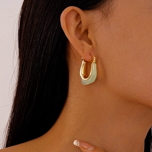 U-shaped gold metal earrings with mint green resin inlay shown on model's ear