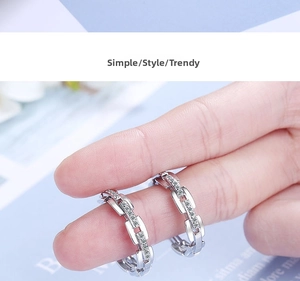Macro view of silver chain earrings with cubic zirconia held by hand for scale
