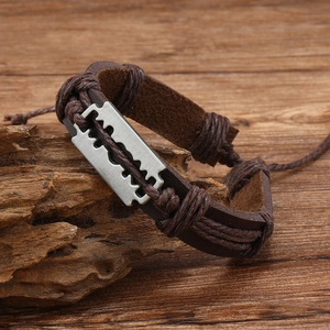 Macro detail of brown braided leather bracelet with vintage silver razor blade charm