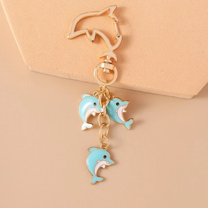 Detail of gold dolphin keychain featuring three blue enamel dolphin charms on geometric stand