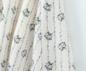 Detailed view of floral fabric with blue daisy patterns on off-white chiffon material