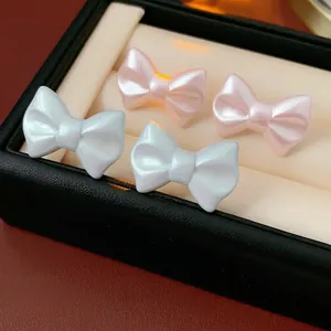 Elegant pearlescent acrylic bow earrings in pearl white and pink on black jewelry display