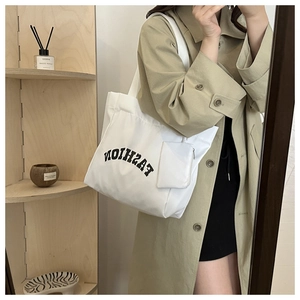 Detail view of a large white canvas tote bag with FASHION print and matching small zipper pouch