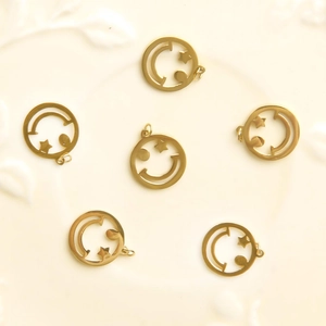 Flat lay of six hollow gold-plated smiley face and star charms on white textured surface