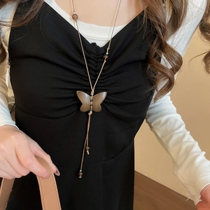 Détail du pendentif papillon en bois marron et des perles sur ce long collier de style bohème