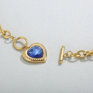 Macro detail of gold-plated OT clasp and blue heart crystal pendant on stainless steel chain