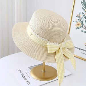 Detail of woven straw hat featuring yellow plaid ribbon, lace trim, and a gold V charm