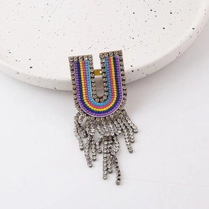 Detail of a U-shaped colorful woven brooch featuring vibrant tassels and sparkly rhinestones